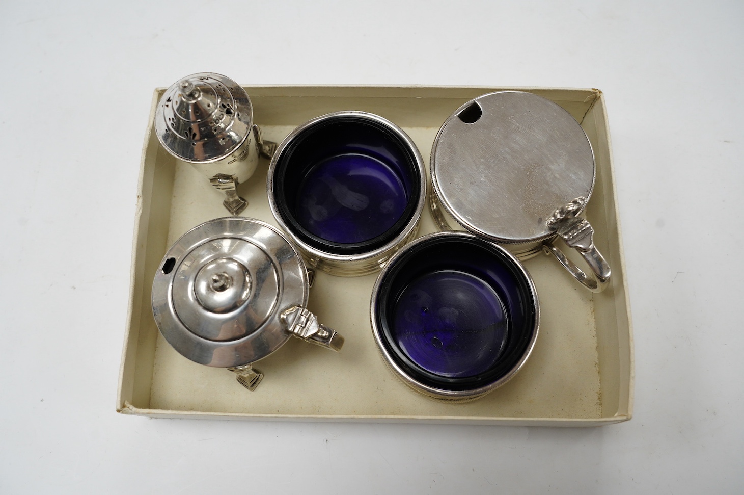 A George V matched silver three piece condiment set, London, 1931(2) and 1933, together with two other silver condiments. Condition - poor to fair